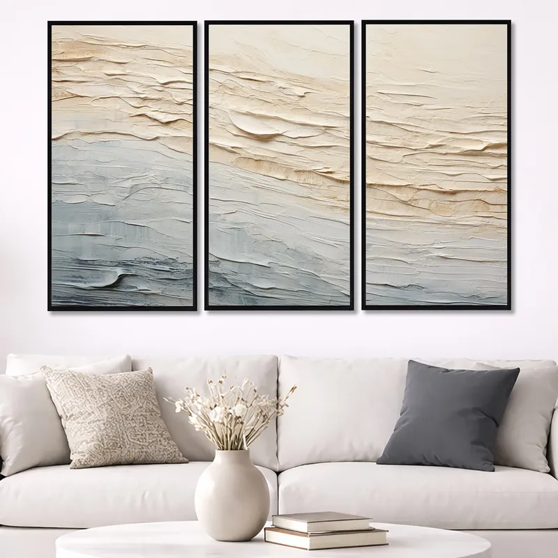 Three framed abstract textured prints in beige and blue hanging above a white sofa